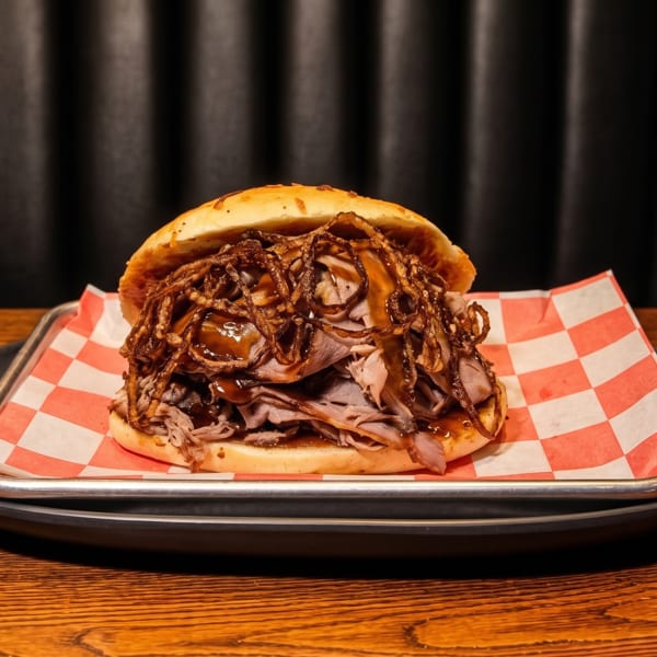 A large roast beef sandwich with crispy fried onions and gravy on a bun.