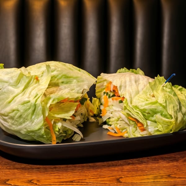 Two lettuce wraps filled with shredded cabbage, carrots, and cucumbers on a dark plate.