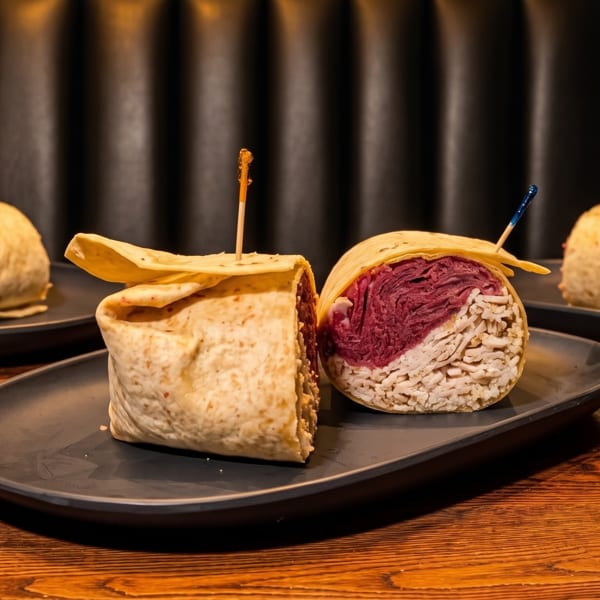 Three wraps on dark plates, one cut open revealing purple and white fillings, on a wooden table.