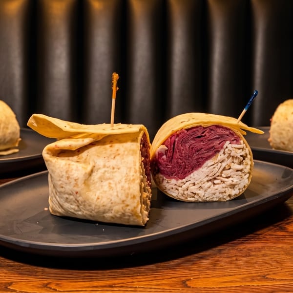 Two wraps, one with red cabbage and white filling, on a dark plate with a wooden table.