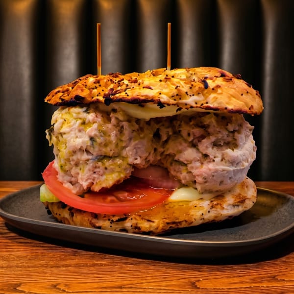 A large tuna salad sandwich with tomato and lettuce on a toasted bun, served on a dark plate.