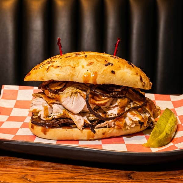 A large, overflowing sandwich with meat, sauce, and crispy onions, served with a pickle spear.